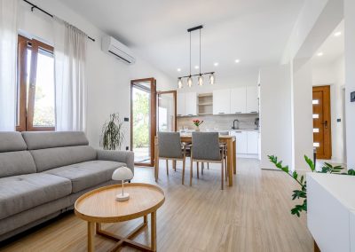 Stol posložen za četvero, kauč u dnevnom boravku i otvorena vrata na terasu našeg šarmantnog apartmana Lumbarda