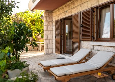 Terasa sa dvije drvene ležaljke s bijelim nadmadracima, kamenim zidovima, drvenim prozorima u šarmantnom apartmanu Lumbarda